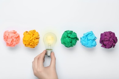Photo of Woman holding lightbulb among colorful paper balls on white background, top view. Idea concept