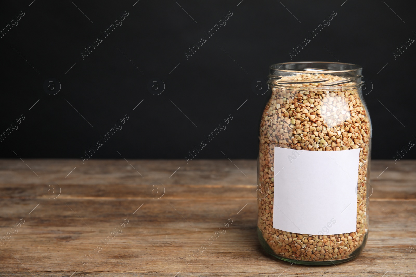 Photo of Organic green buckwheat in jar with blank label on wooden table. Space for text