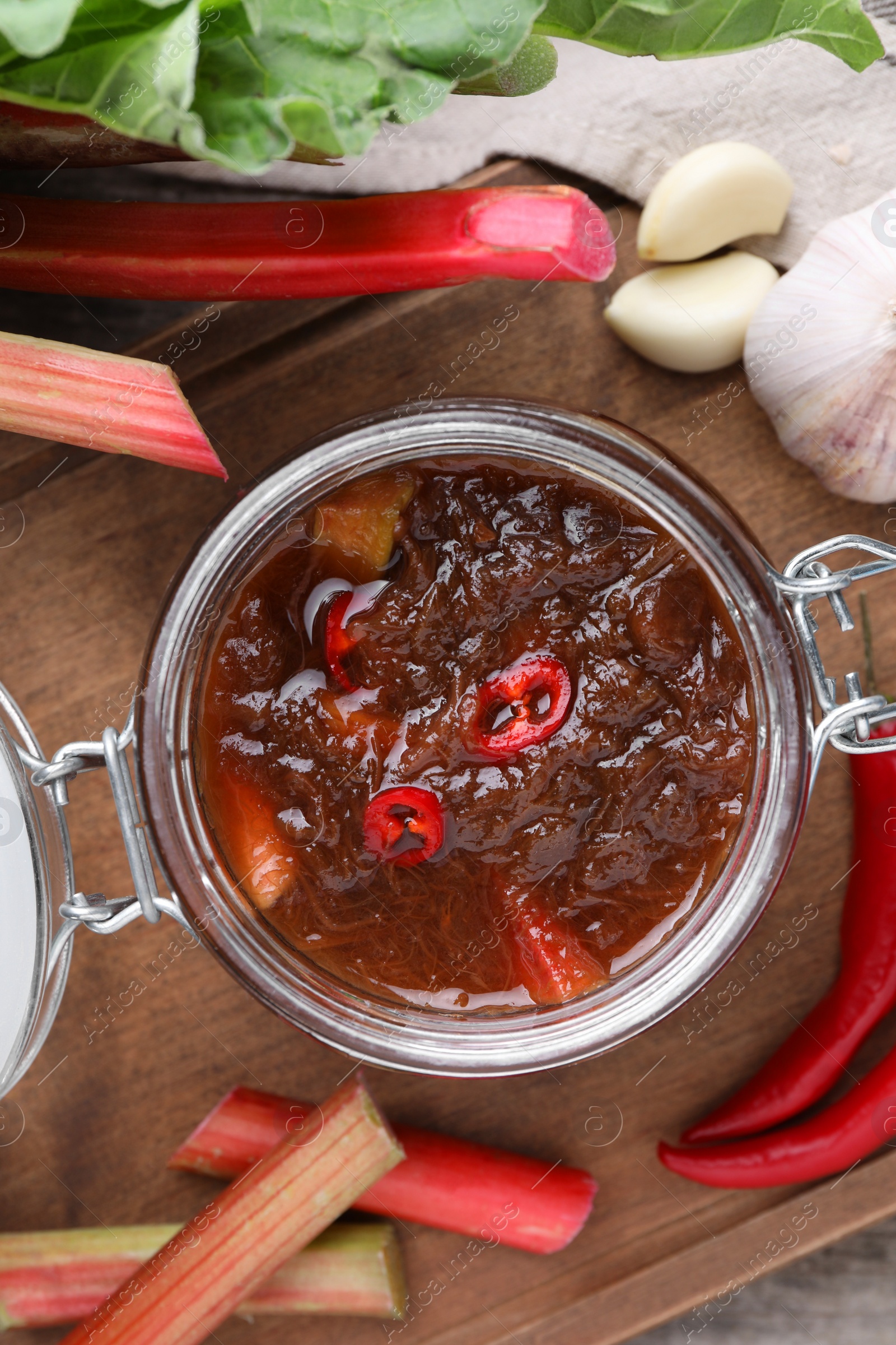 Photo of Tasty rhubarb sauce and ingredients on wooden board, flat lay