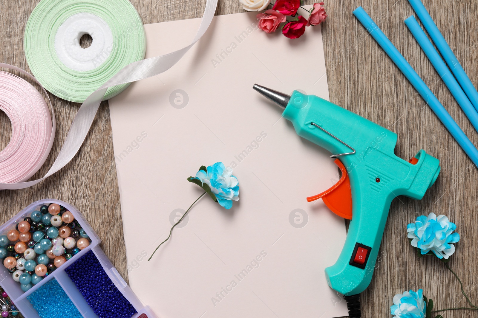 Photo of Hot glue gun and handicraft materials on wooden table, flat lay