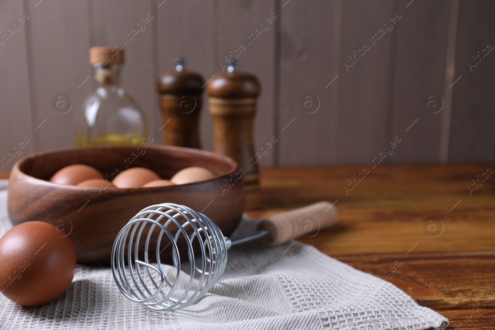 Photo of Making dough. Metal whisk and eggs in wooden bowl on table, closeup