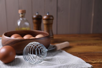 Photo of Making dough. Metal whisk and eggs in wooden bowl on table, closeup