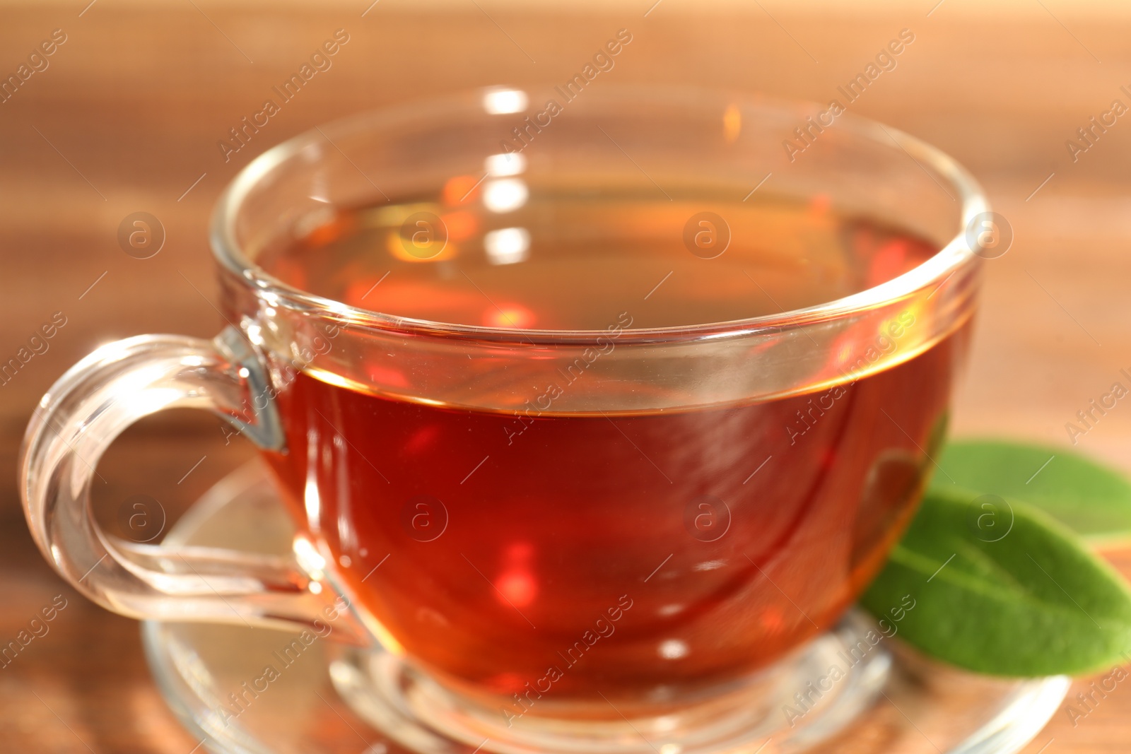 Photo of Aromatic tea in glass cup and green leaves on wooden table, closeup