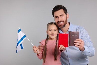 Immigration. Happy man with his daughter holding passports and flag of Israel on gray background