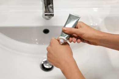 Photo of Woman applying hand cream over sink in bathroom, closeup