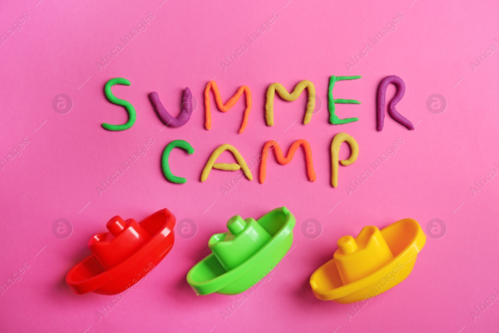 Photo of Flat lay composition with words SUMMER CAMP made from modelling clay and plastic boats on color background