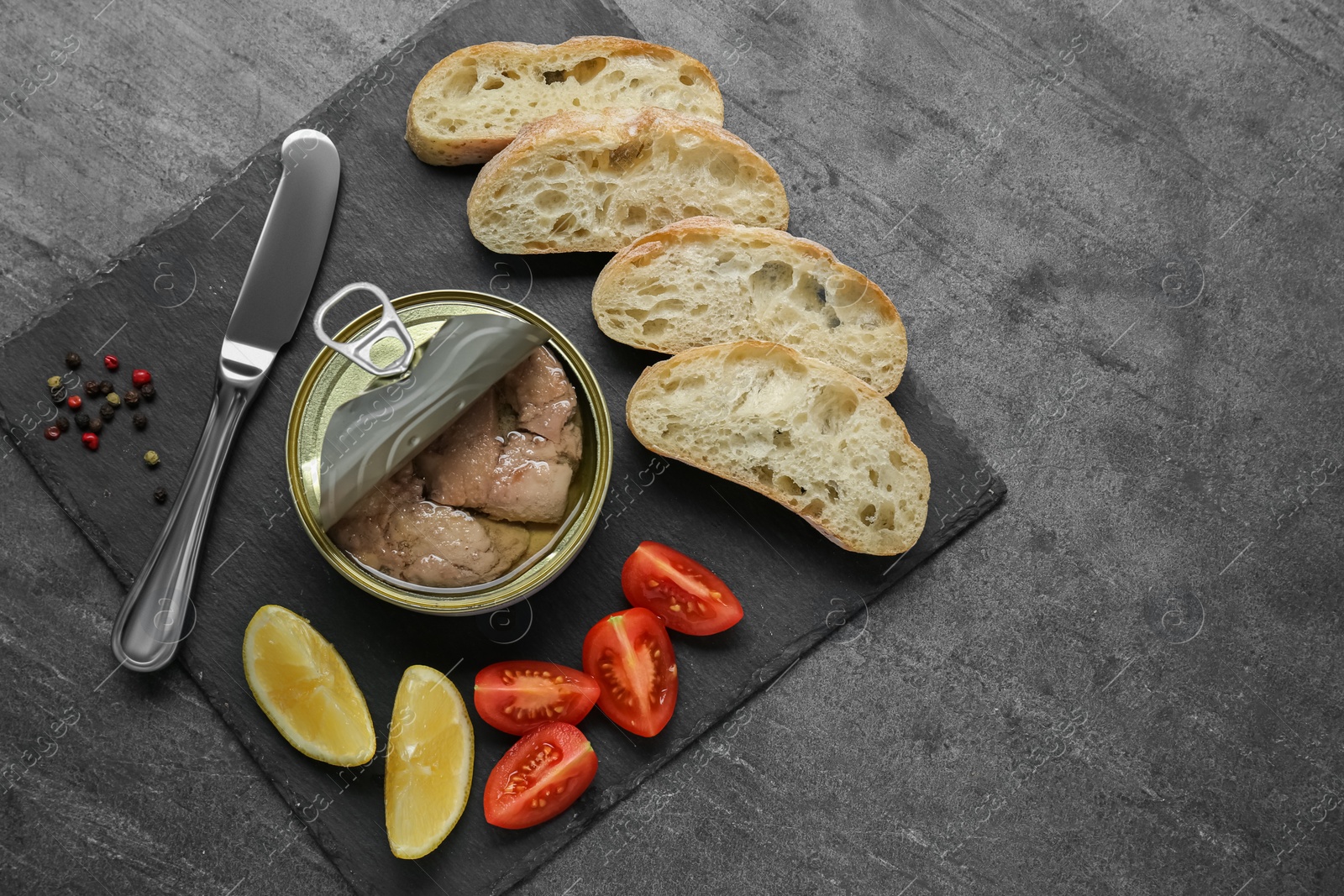 Photo of Flat lay composition with tin can of tasty cod liver and different products on black table. Space for text