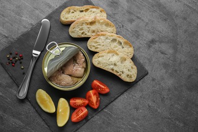 Photo of Flat lay composition with tin can of tasty cod liver and different products on black table. Space for text