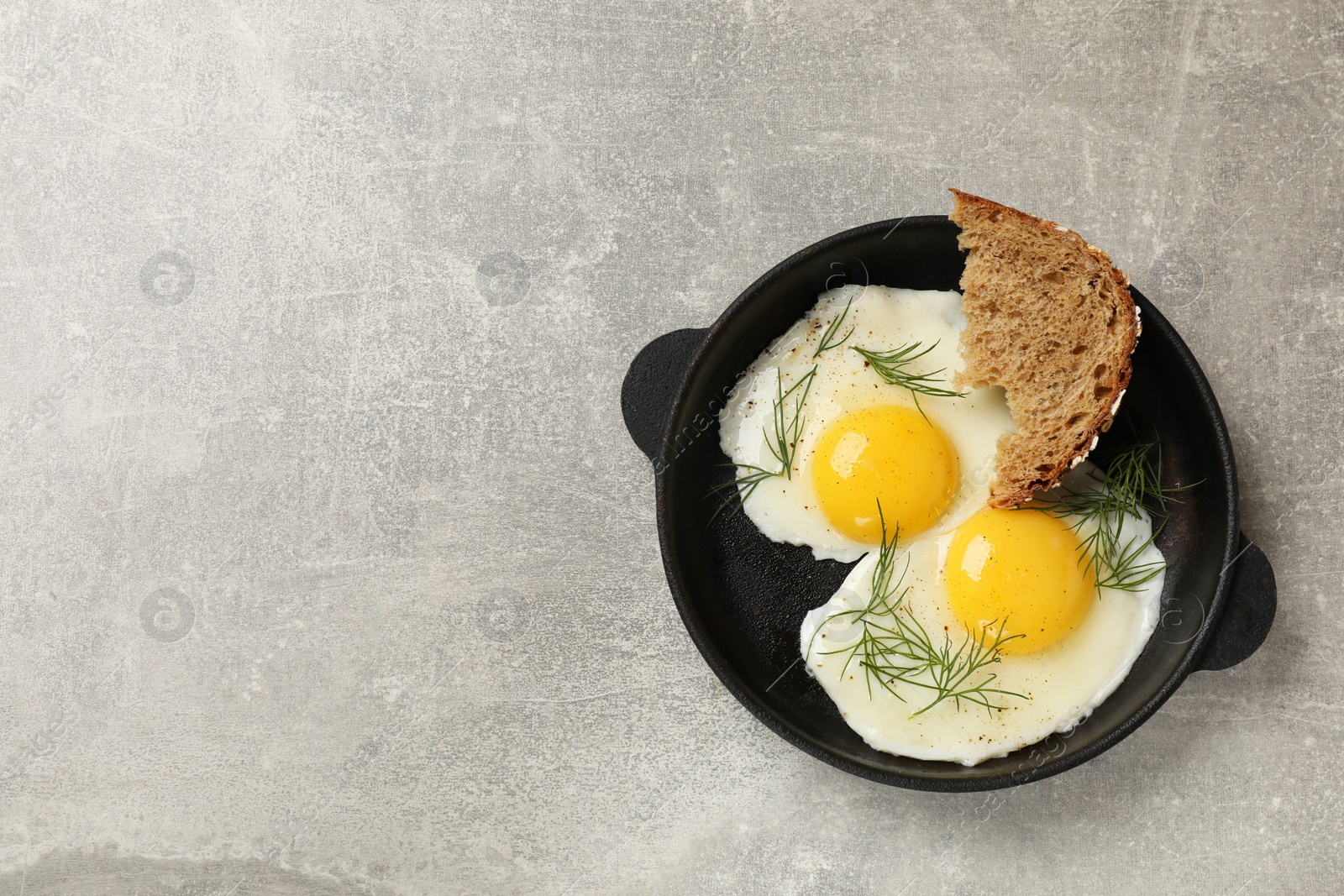 Photo of Delicious fried eggs served with bread on grey table, top view. Space for text