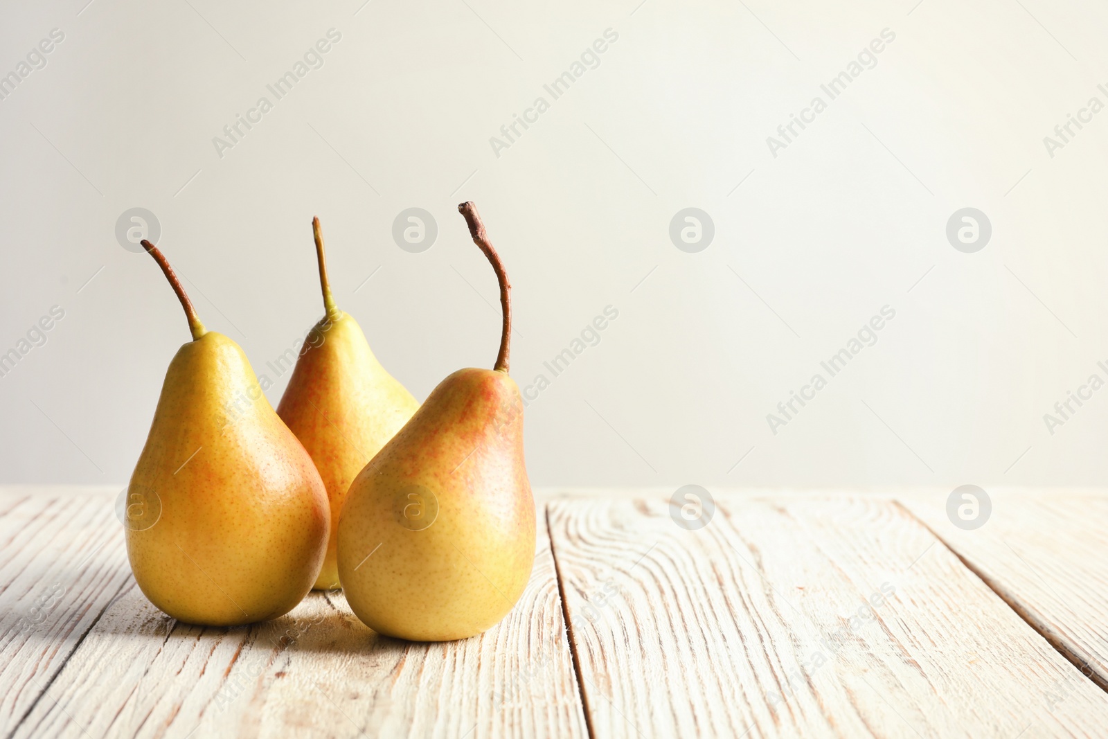 Photo of Ripe pears on wooden table against light background. Space for text