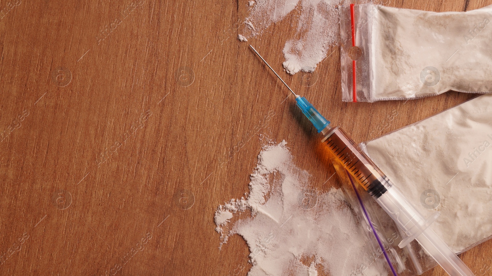 Photo of Plastic bags of powder and syringe on wooden table, flat lay with space for text. Hard drugs