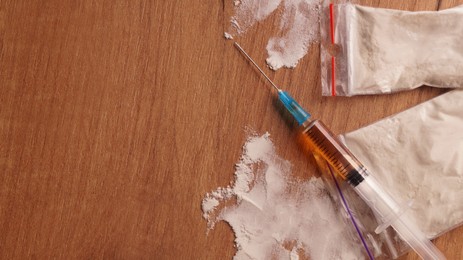 Plastic bags of powder and syringe on wooden table, flat lay with space for text. Hard drugs
