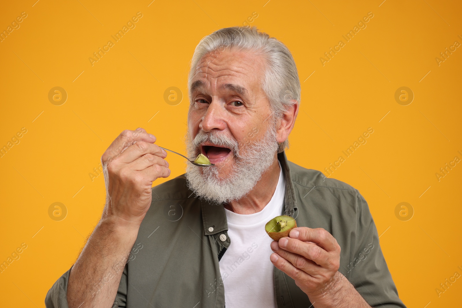 Photo of Senior man eating kiwi with spoon on yellow background
