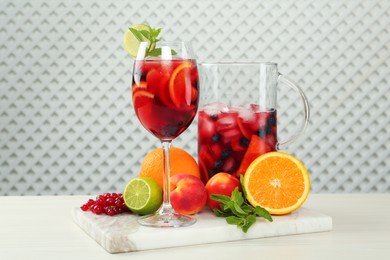 Glass and jug of Red Sangria with fruits on white wooden table