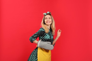 Photo of Young housewife with hair curlers on red background