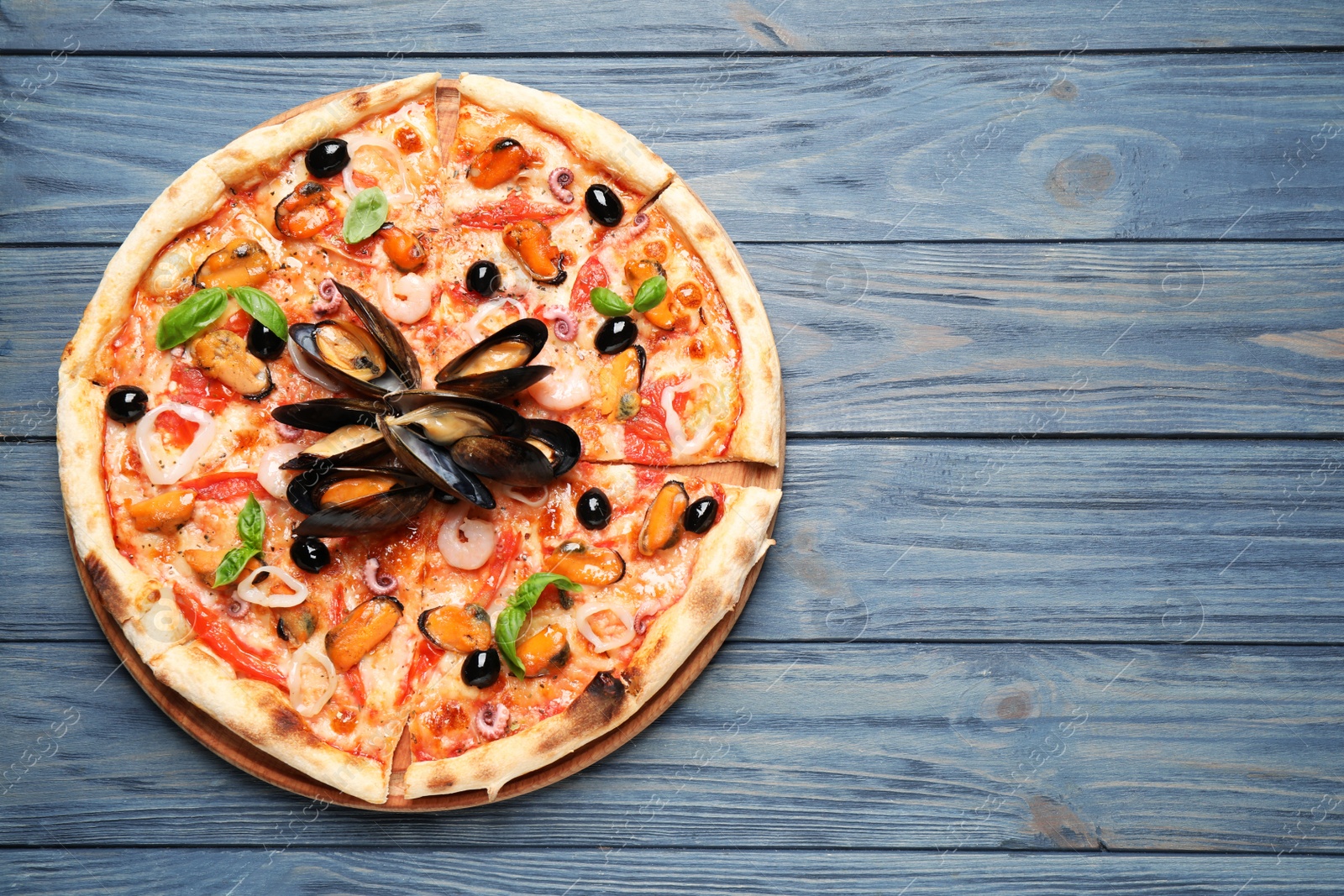 Photo of Tasty pizza with seafood and fresh basil on blue wooden table, top view. Space for text