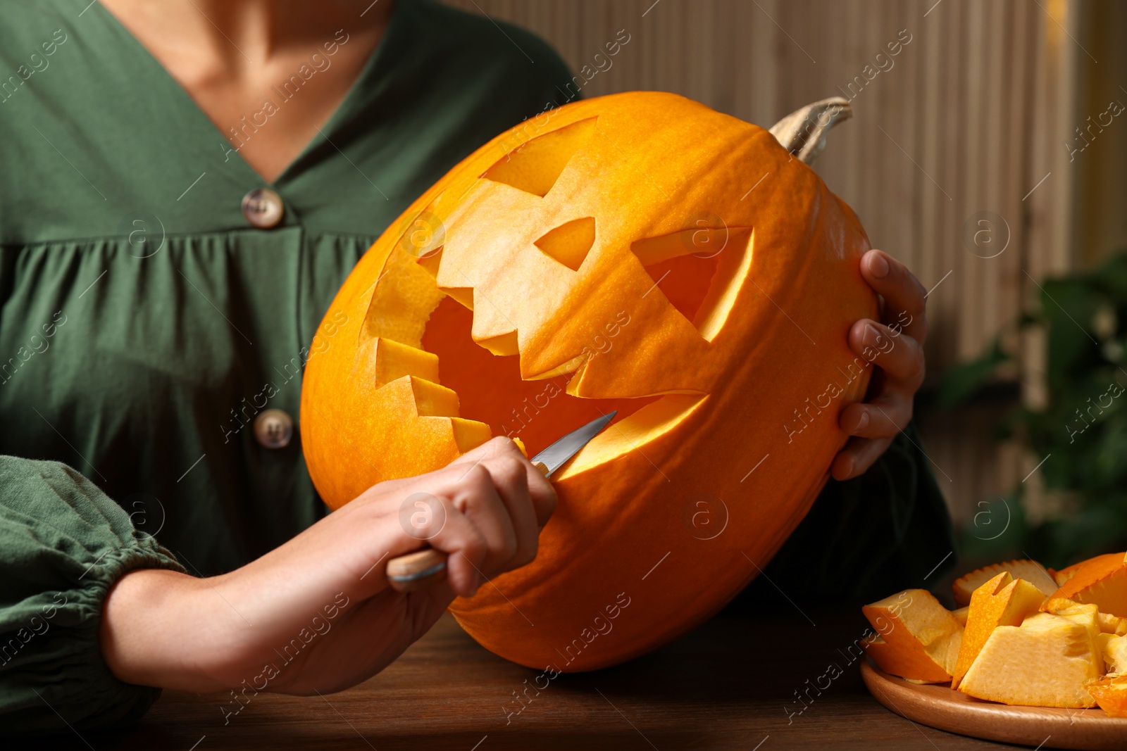 Photo of Woman carving pumpkin for Halloween at wooden table, closeup