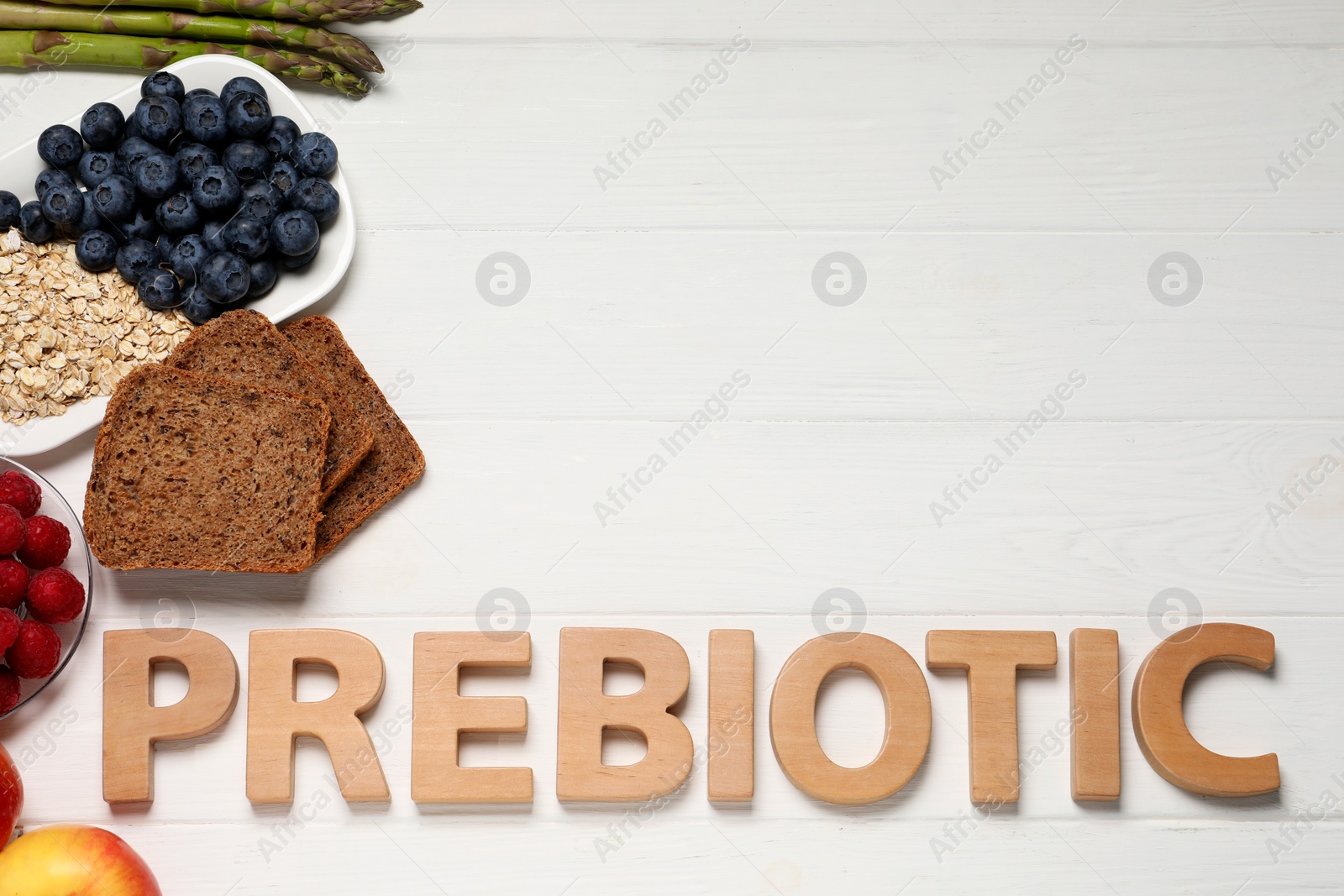 Photo of Word Prebiotic made of letters and foodstuff on white wooden table, flat lay. Space for text