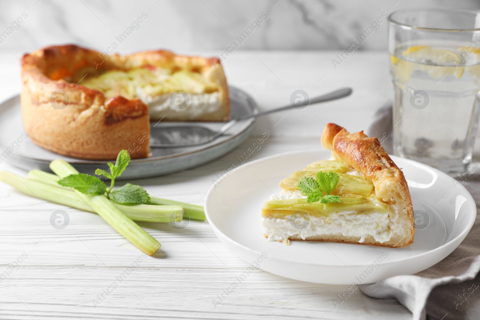 Photo of Freshly baked rhubarb pie with cream cheese, stalks and mint leaves on white wooden table