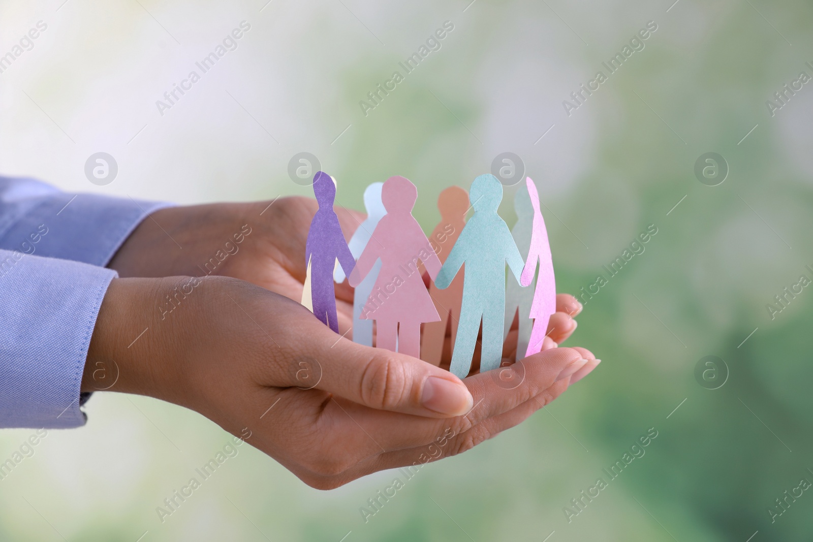 Photo of Woman holding paper human figures on blurred background, closeup. Diversity and Inclusion concept