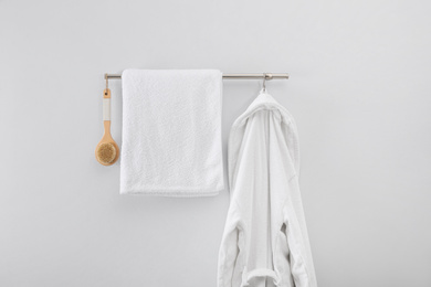 Photo of Rack with clean bathrobe, brush and towel on light wall