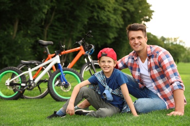 Dad and son sitting near their bicycles outdoors