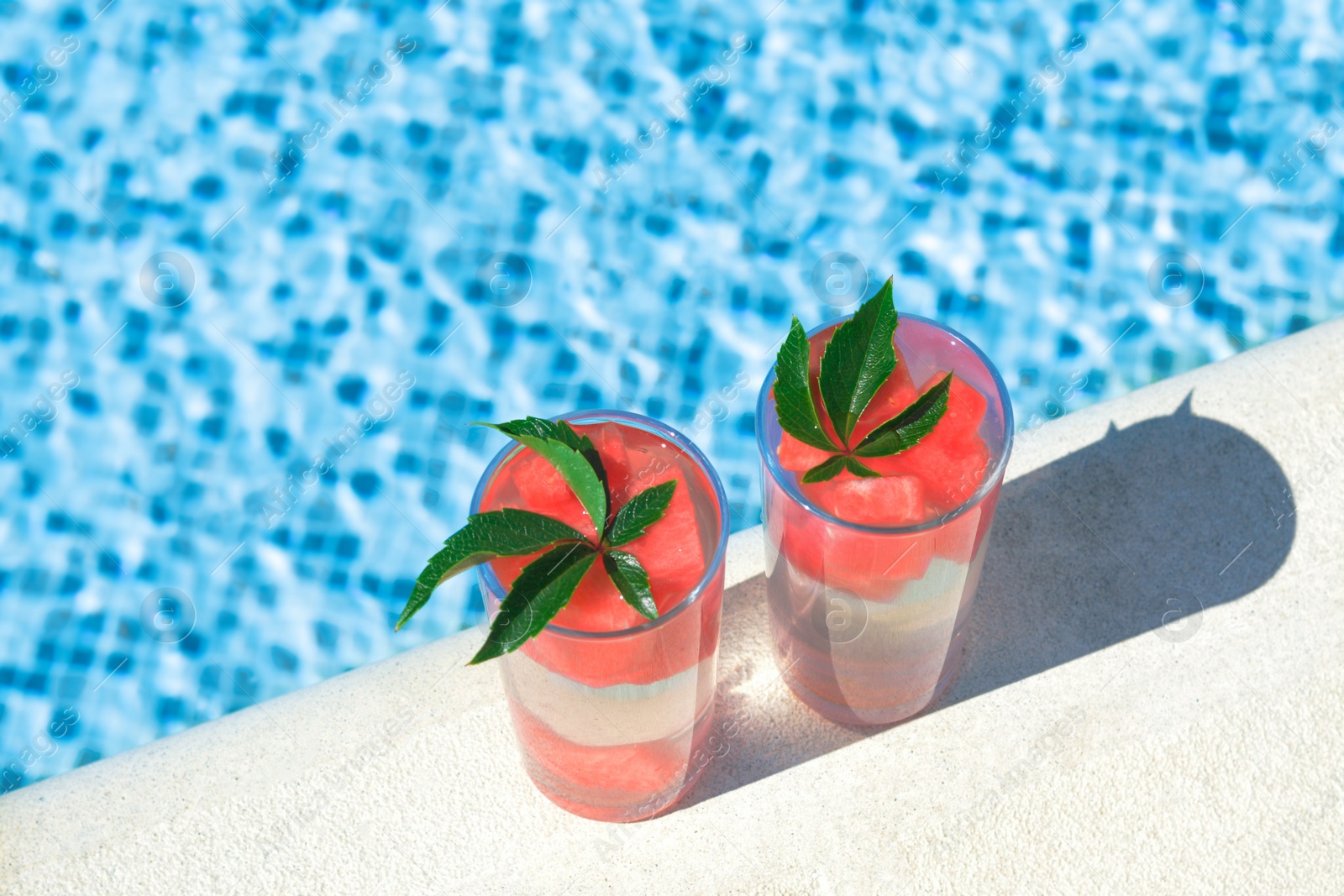 Photo of Refreshing watermelon drink in glasses near swimming pool outdoors. Space for text