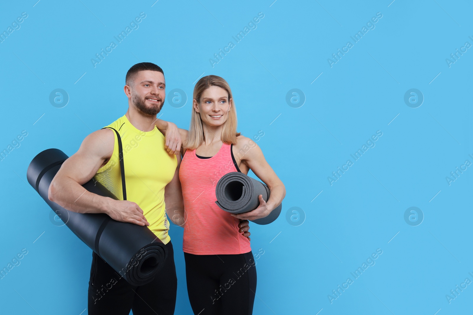 Photo of Athletic people with fitness mats on light blue background, space for text