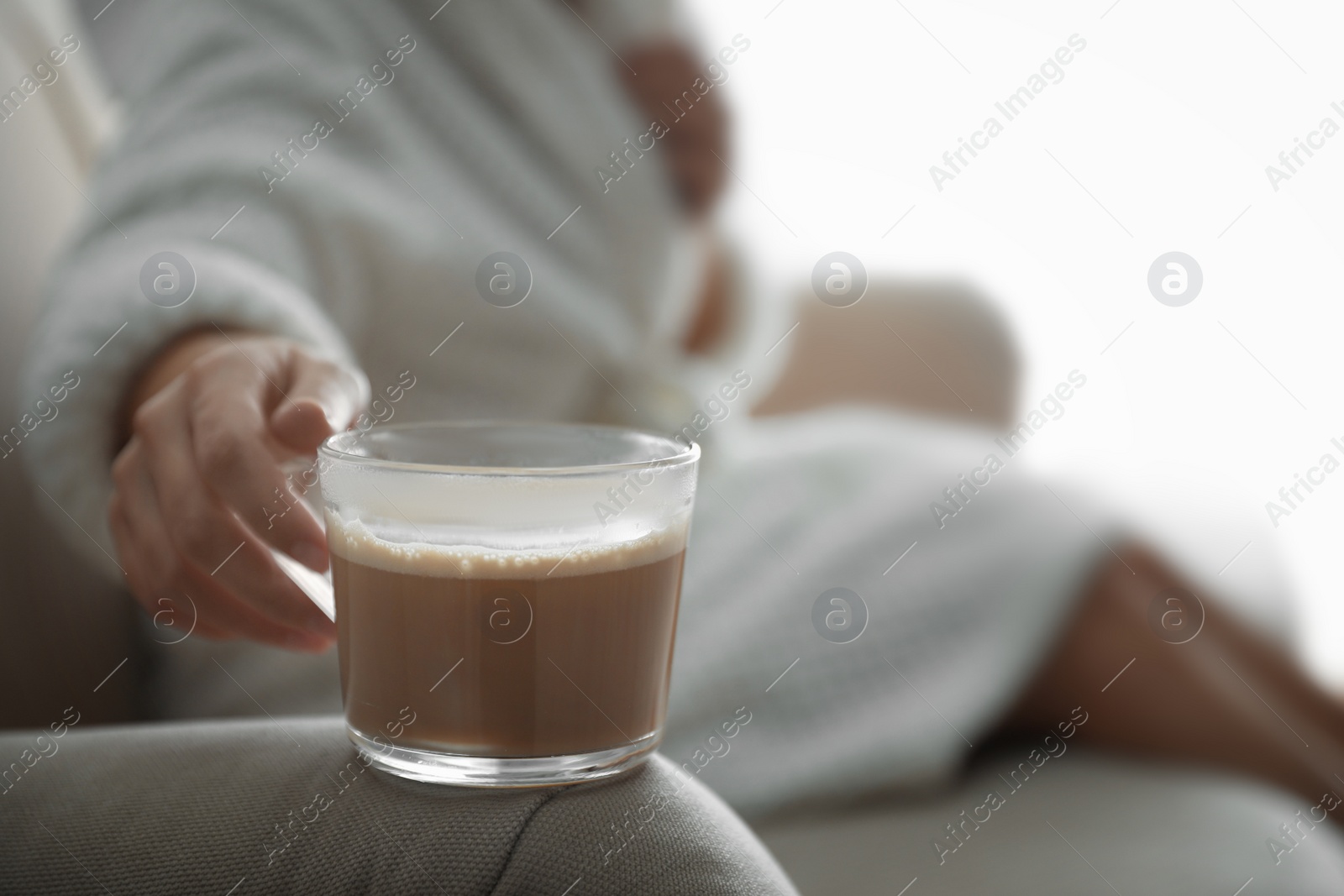 Photo of Woman with cup of hot drink on sofa at home in morning, closeup. Space for text