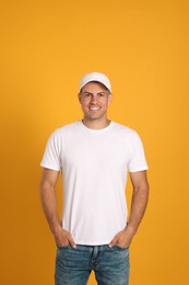 Photo of Happy man in white cap and tshirt on yellow background. Mockup for design