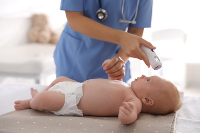 Photo of Doctor measuring temperature of little baby with non-contact thermometer in clinic, closeup. Health care