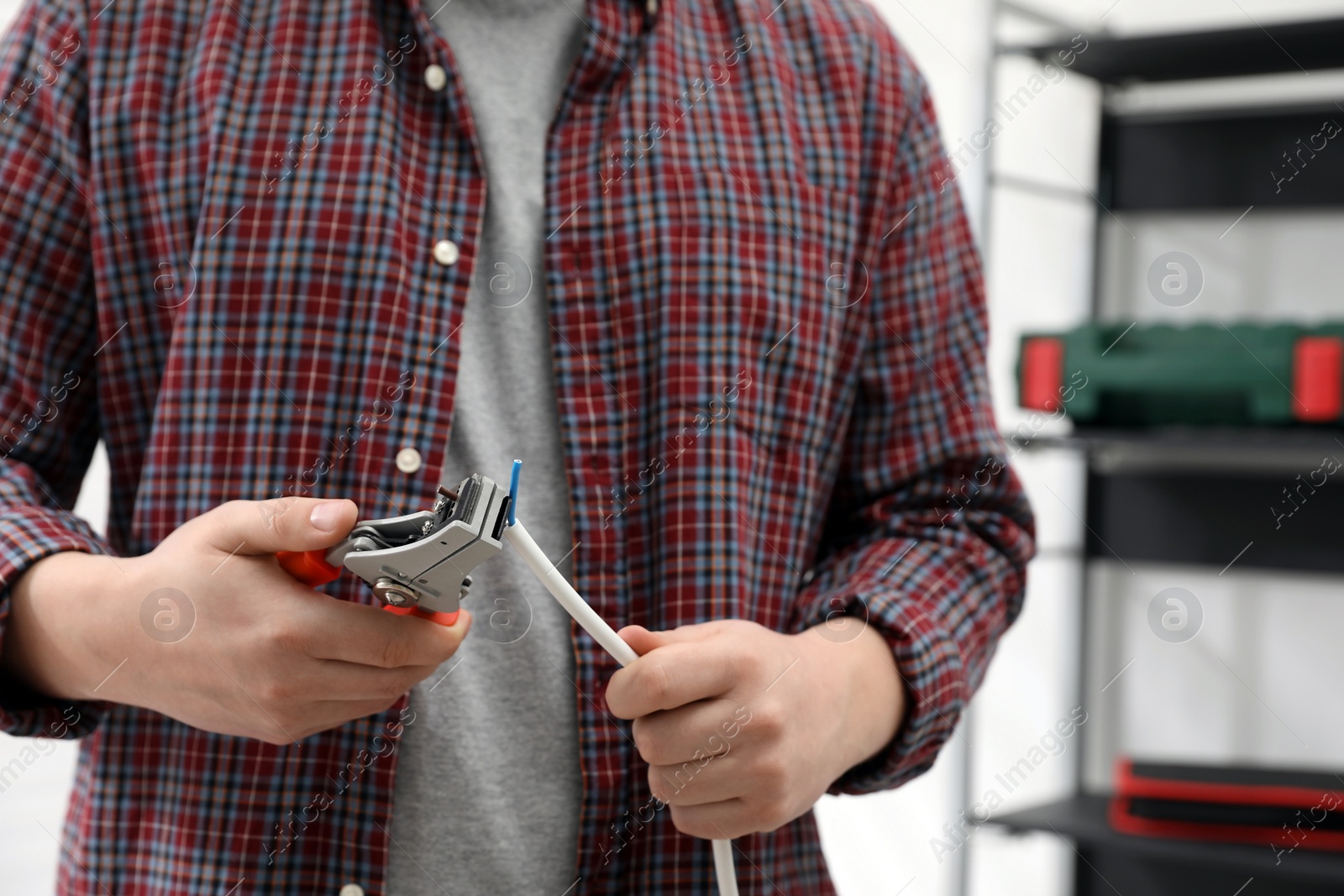 Photo of Professional electrician stripping wiring indoors, closeup view