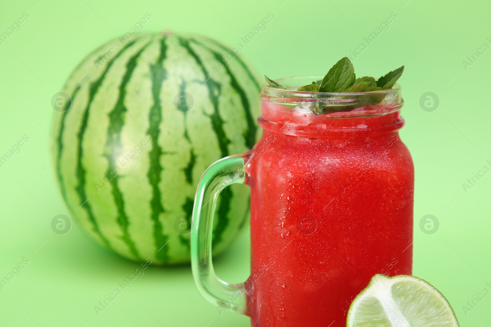 Photo of Glass of delicious watermelon drink with mint and fresh fruits on light green background, closeup