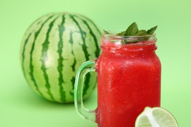 Photo of Glass of delicious watermelon drink with mint and fresh fruits on light green background, closeup