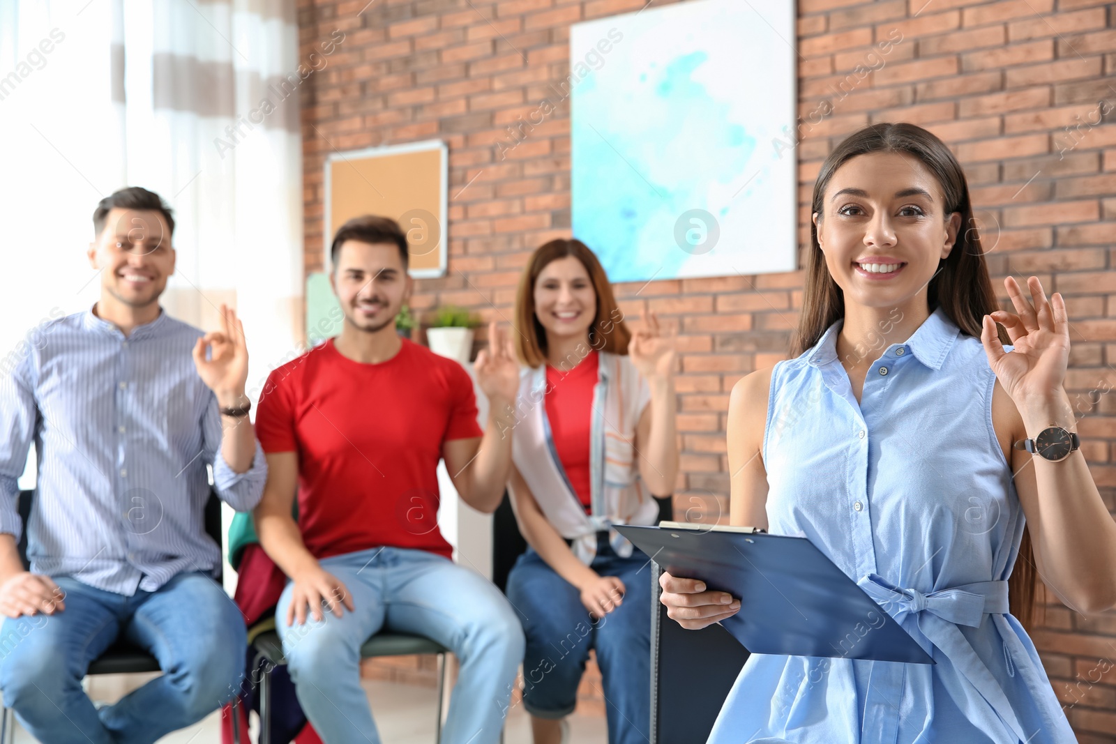 Photo of Young teacher showing sign language gesture against blurred background