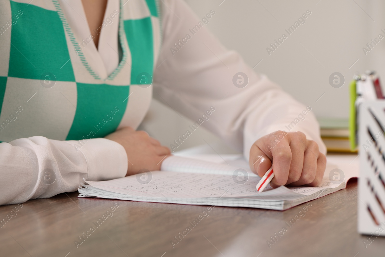 Photo of Girl erasing mistake in her notebook at wooden desk, closeup