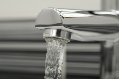 Water flowing from tap on blurred background, closeup