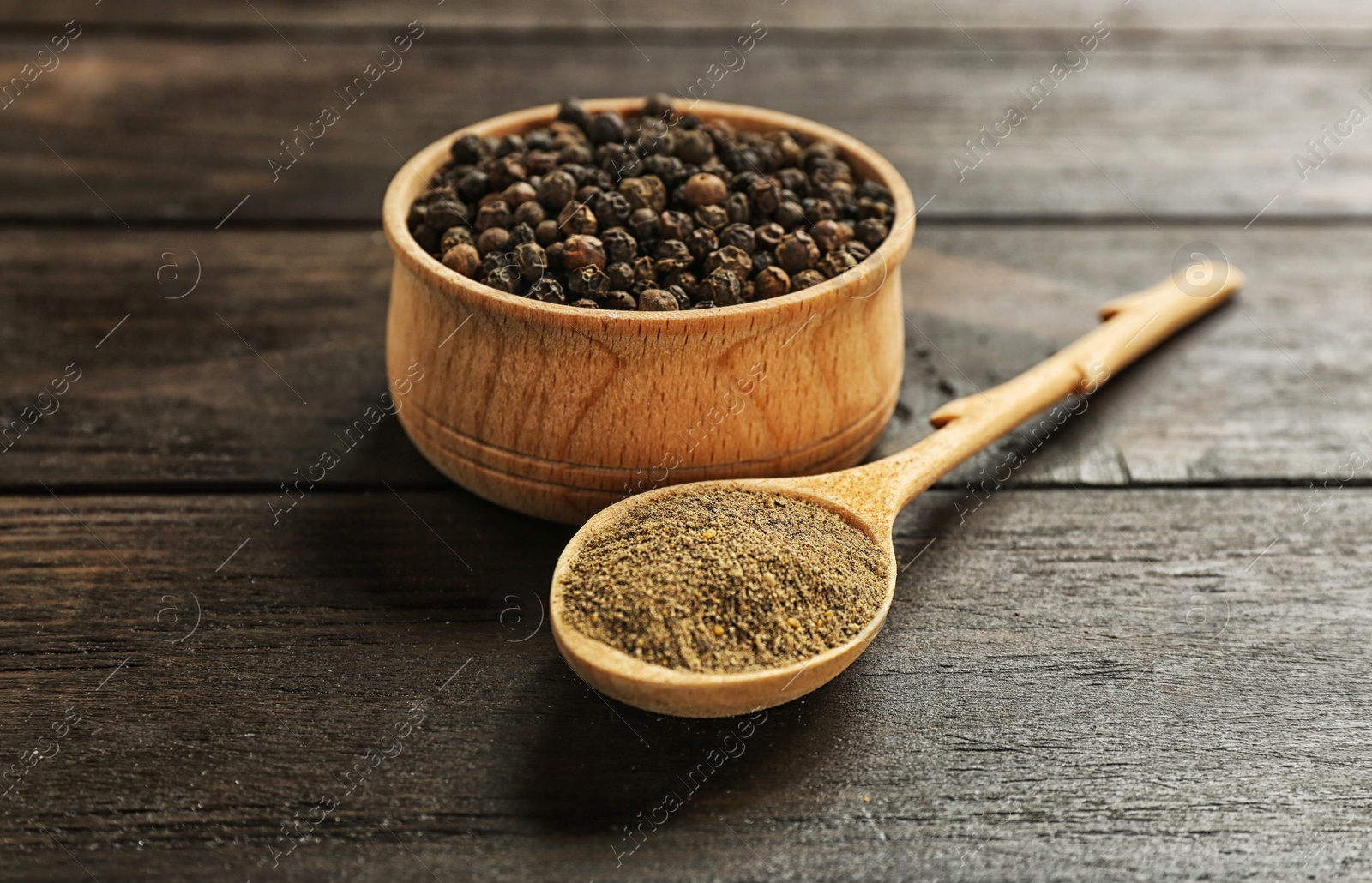 Photo of Spoon with powdered black pepper and corns in bowl on wooden table