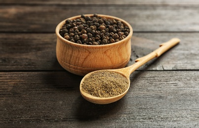 Photo of Spoon with powdered black pepper and corns in bowl on wooden table