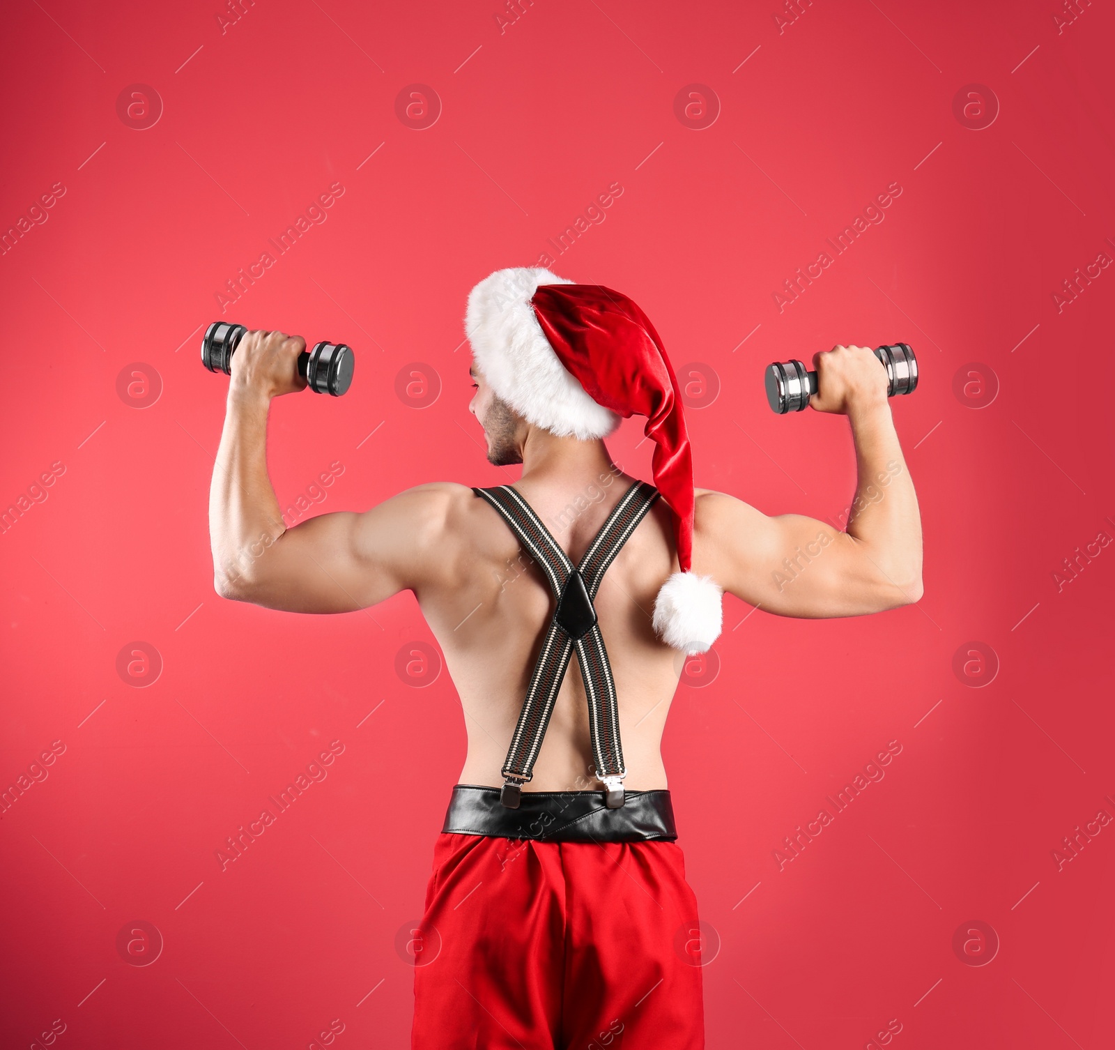 Photo of Shirtless sexy young Santa Claus with dumbbells on color background