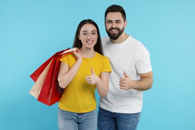 Photo of Happy couple with shopping bags showing thumbs up on light blue background