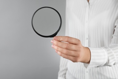 Photo of Woman holding magnifying glass on grey background, closeup. Find keywords concept