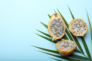 Photo of Delicious cut dragon fruits (pitahaya) and tropical leaf on light blue background, flat lay. Space for text