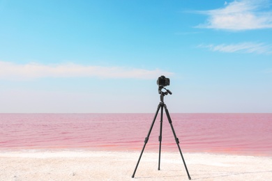 Professional camera on tripod near pink lake