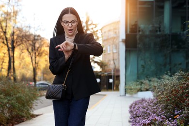 Emotional woman checking time on watch outdoors. Being late concept