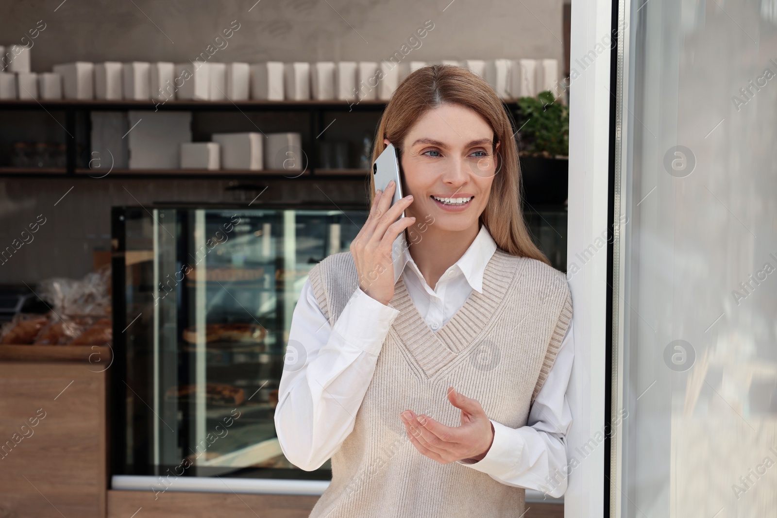 Photo of Happy business owner talking on phone in bakery shop. Space for text