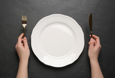 Woman with empty plate and cutlery at black table, top view