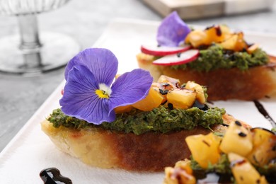 Photo of Delicious bruschettas with pesto sauce, tomatoes, balsamic vinegar and violet flower on gray table, closeup