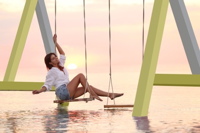 Photo of Young woman enjoying sunrise on swing over water