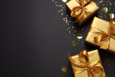 Photo of Golden gift boxes and confetti on black background, flat lay. Space for text